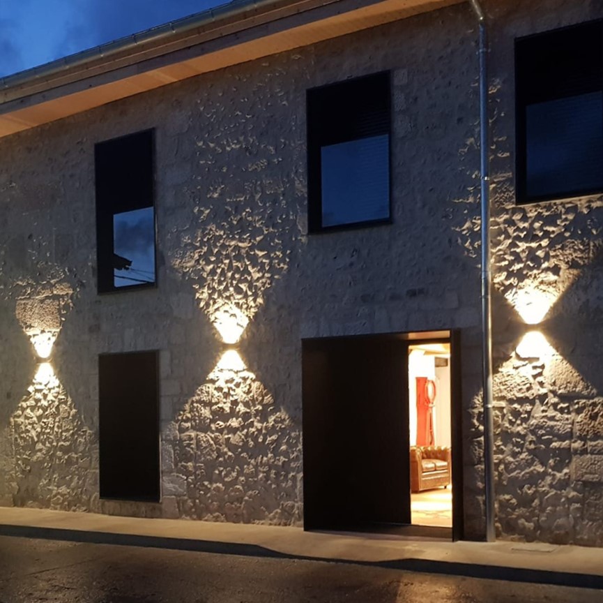 Fachada de piedra iluminada de noche con apliques de doble haz
