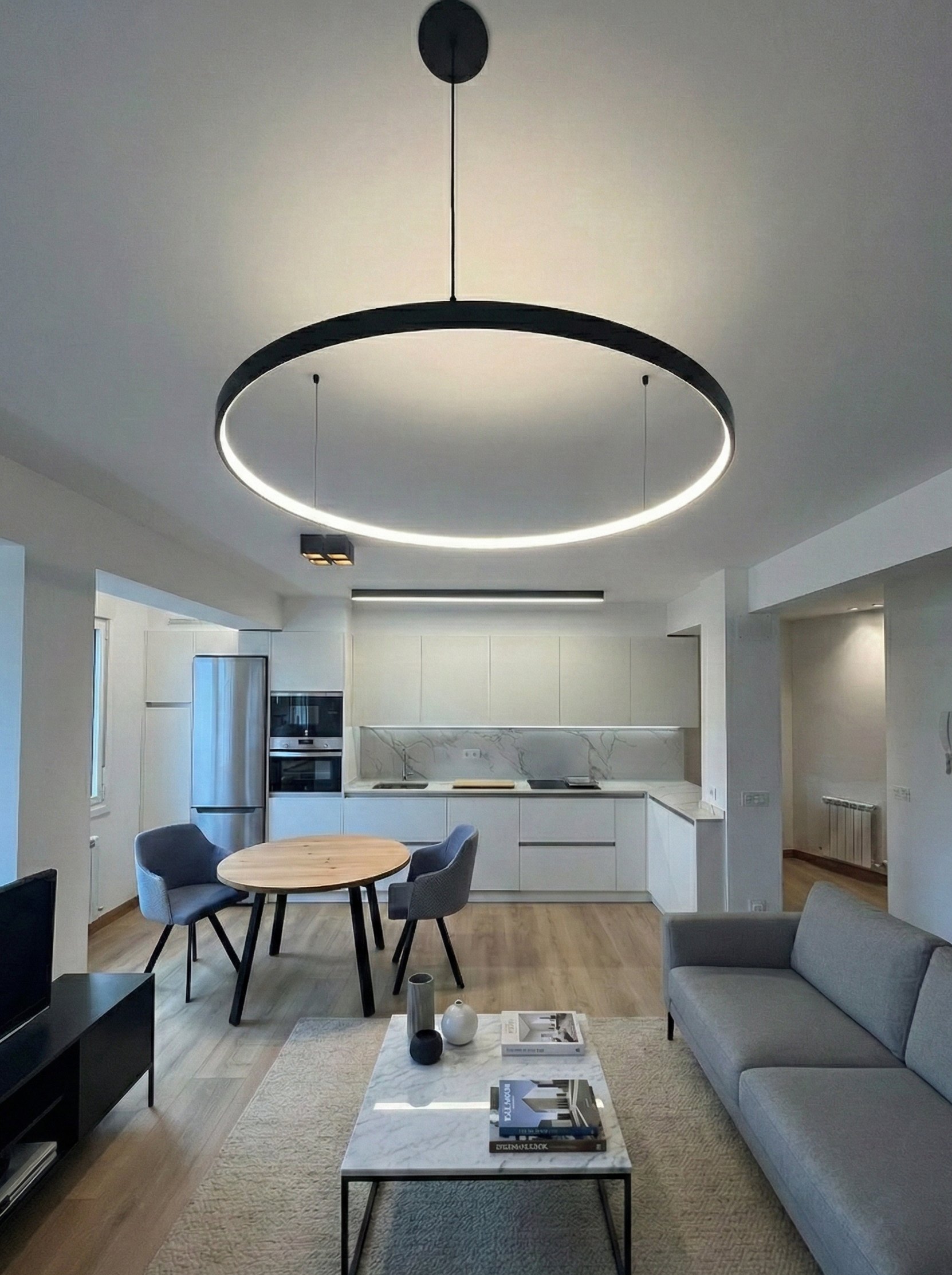 Salón abierto con gran aro LED suspendido y cocina al fondo